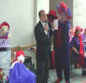 Queen Jill placing a red hat on the Mayor's head.